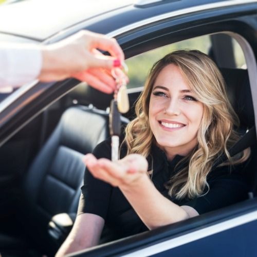 Woman smiling in a car as someone hands her keys through the open window