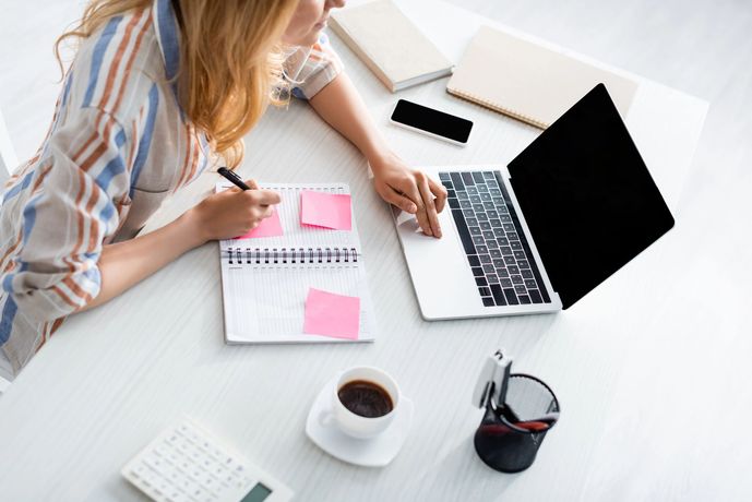 Persona trabajando en un escritorio con una computadora portátil, un cuaderno, notas adhesivas, café y auriculares.