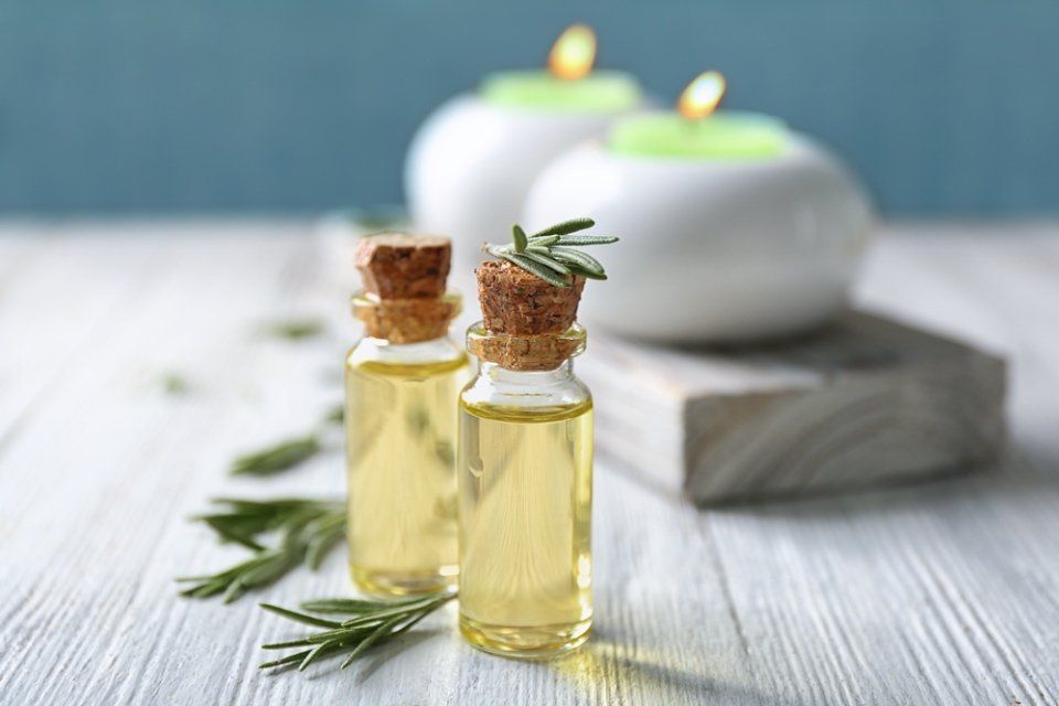 Due bottiglie di vetro di olio con rametti di rosmarino, candele, su legno bianco.