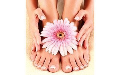 Mani che tengono un fiore rosa sopra i piedi curati.
