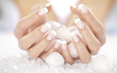 Mani con unghie alla francese che racchiudono pietre bianche.