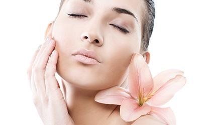 Donna con gli occhi chiusi, che si tocca delicatamente il viso, con un fiore rosa vicino al collo.