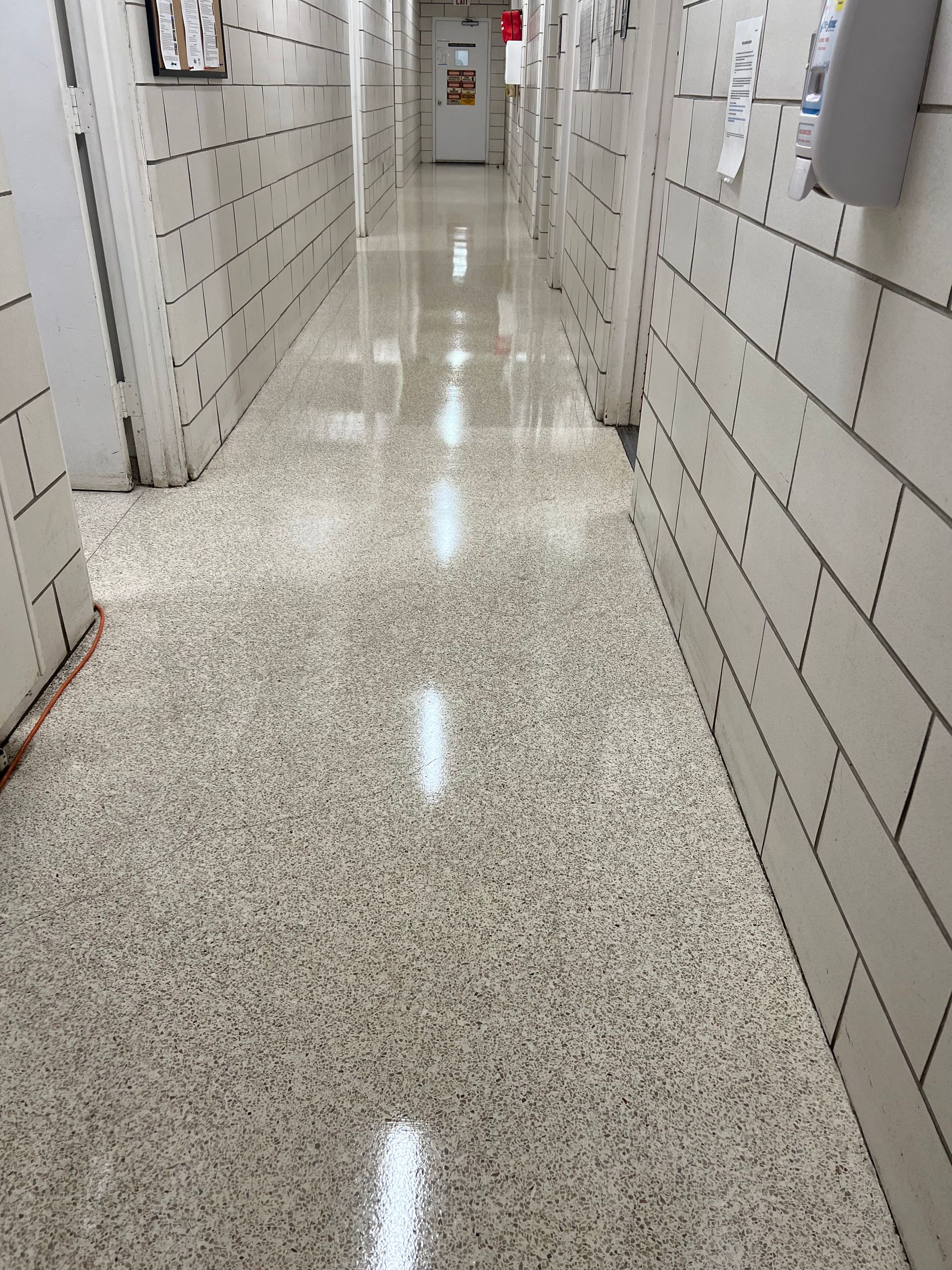 A long hallway with white brick walls and a shiny floor
