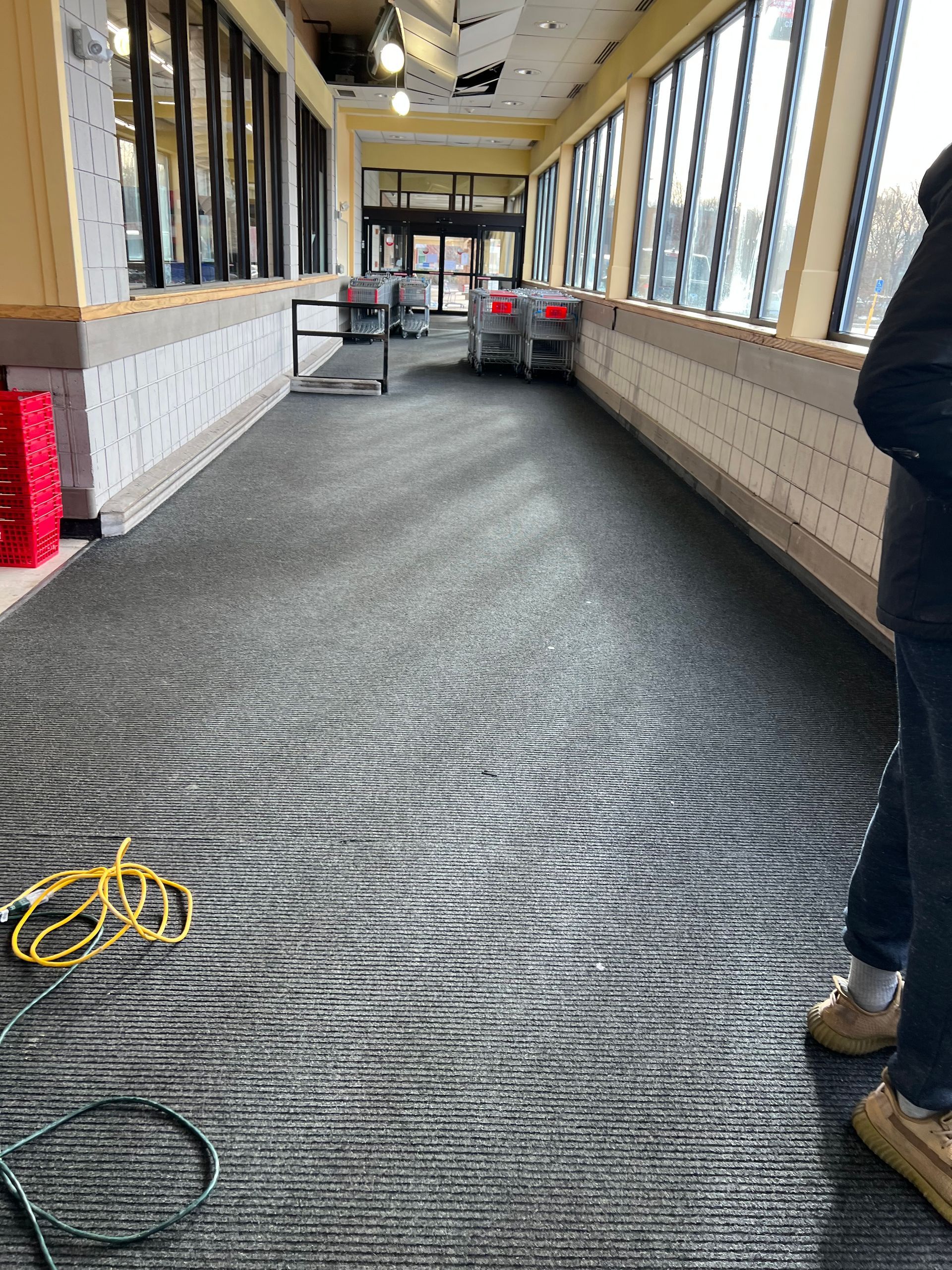 A person is standing in a long hallway with a carpeted floor.
