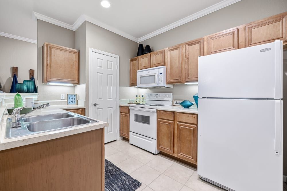 Chef-inspired kitchen with wooden cabinets, a white refrigerator, stove, microwave and sink at Marquis at The Cascades in Tyler, TX.