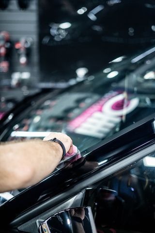 A person is cleaning the windshield of a car with a cloth.