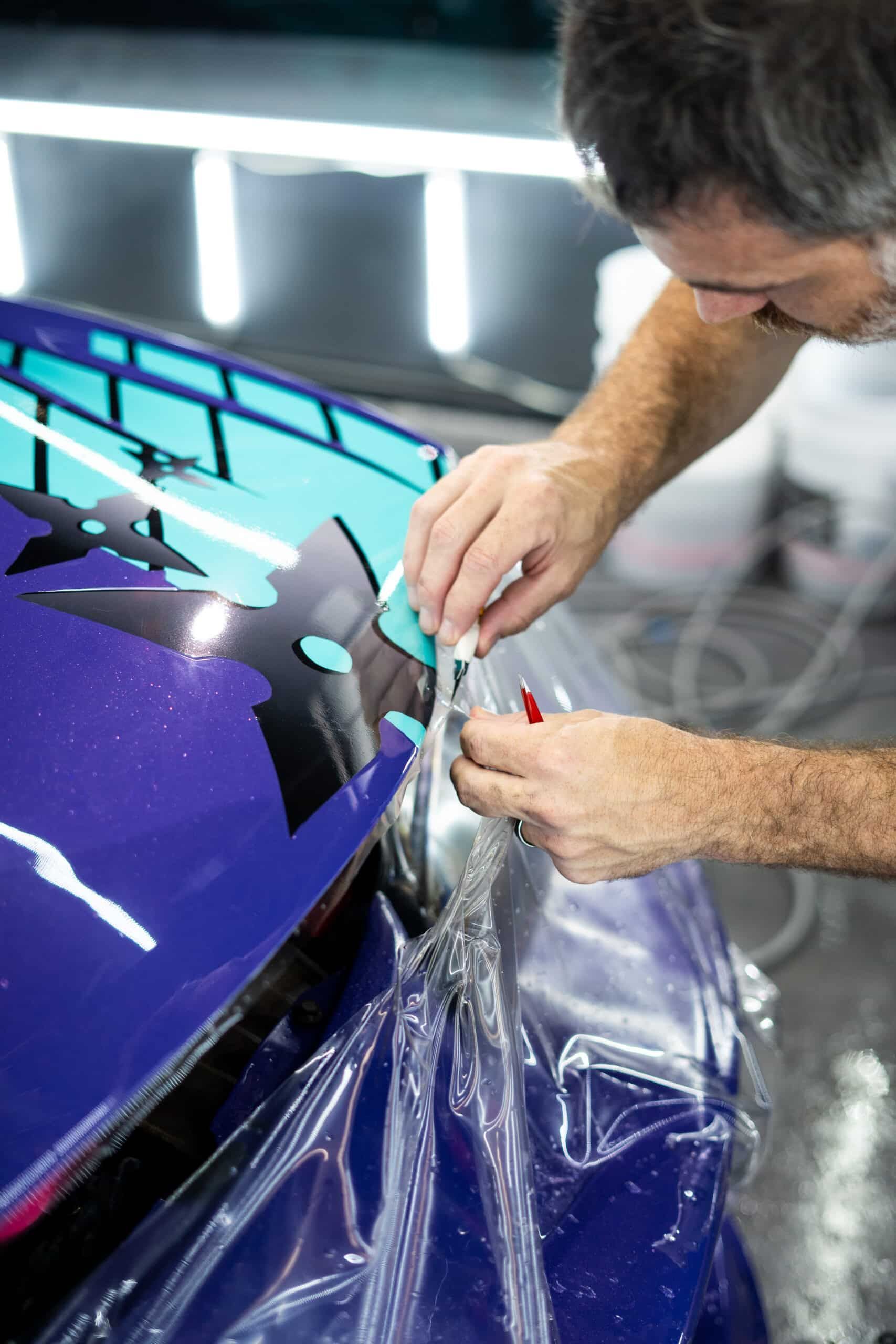A man is wrapping a purple car with plastic wrap.