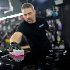 A man is cleaning a car with a sponge in a garage.