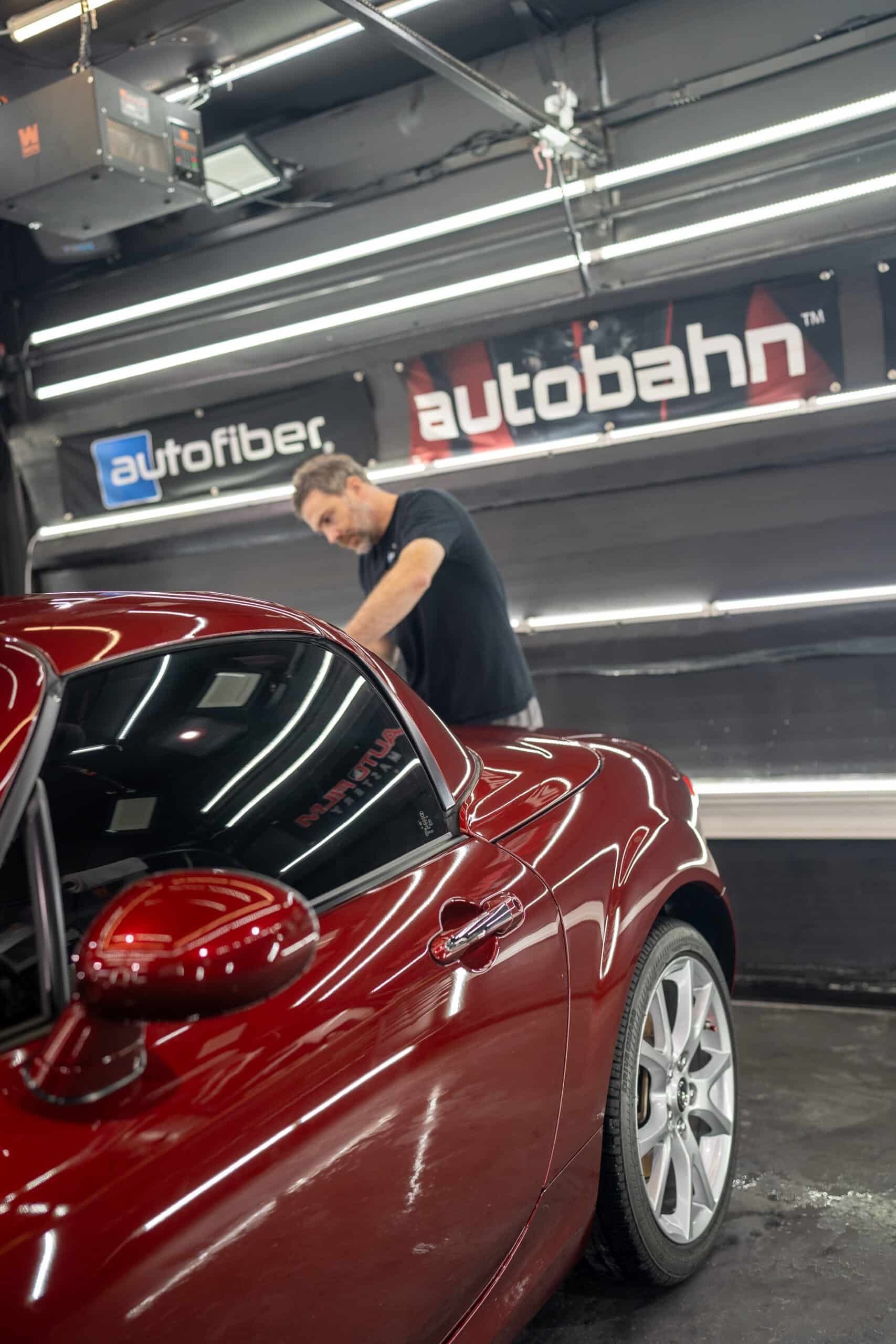 A man is standing next to a red car in a garage.