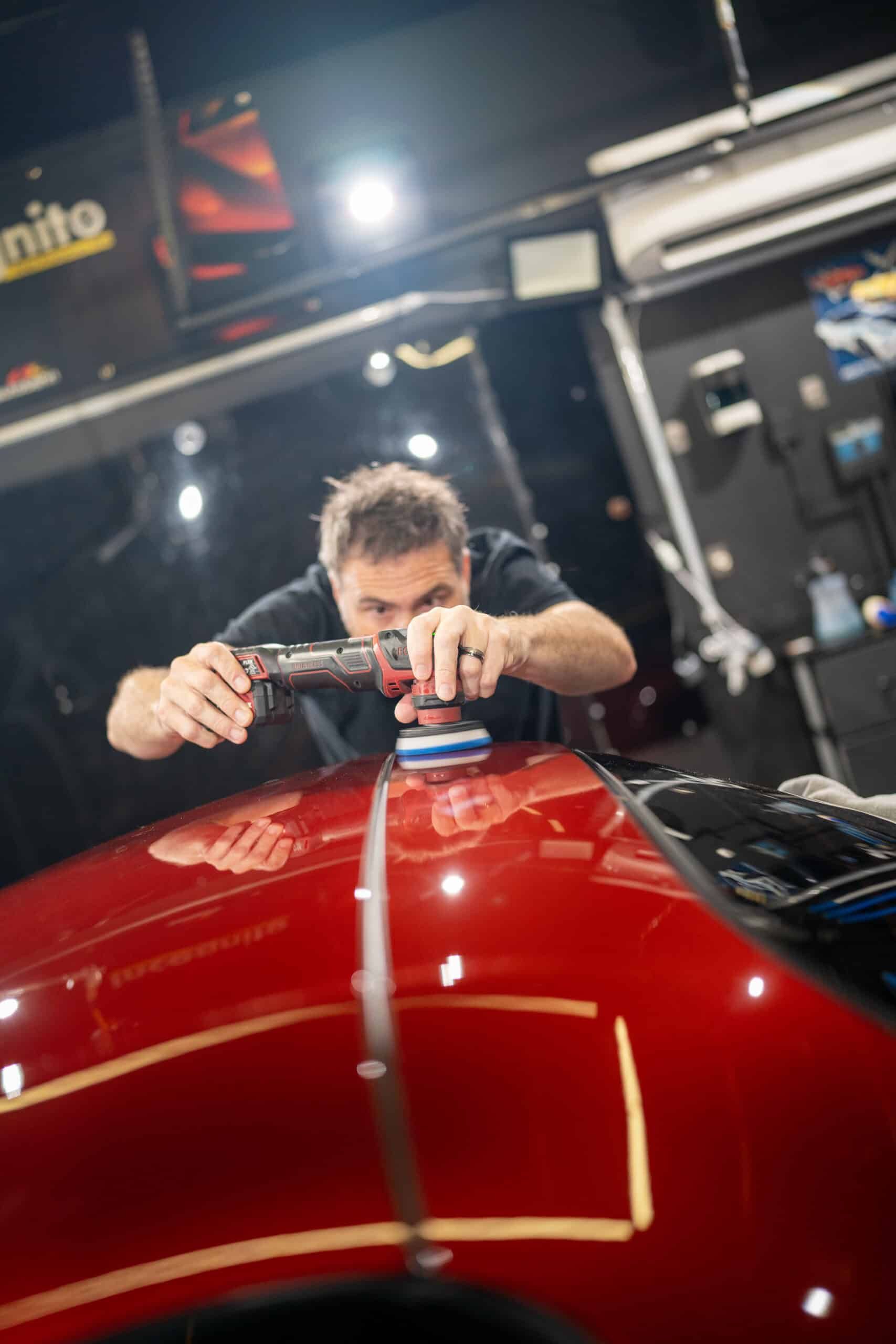 A man is polishing the hood of a red car.