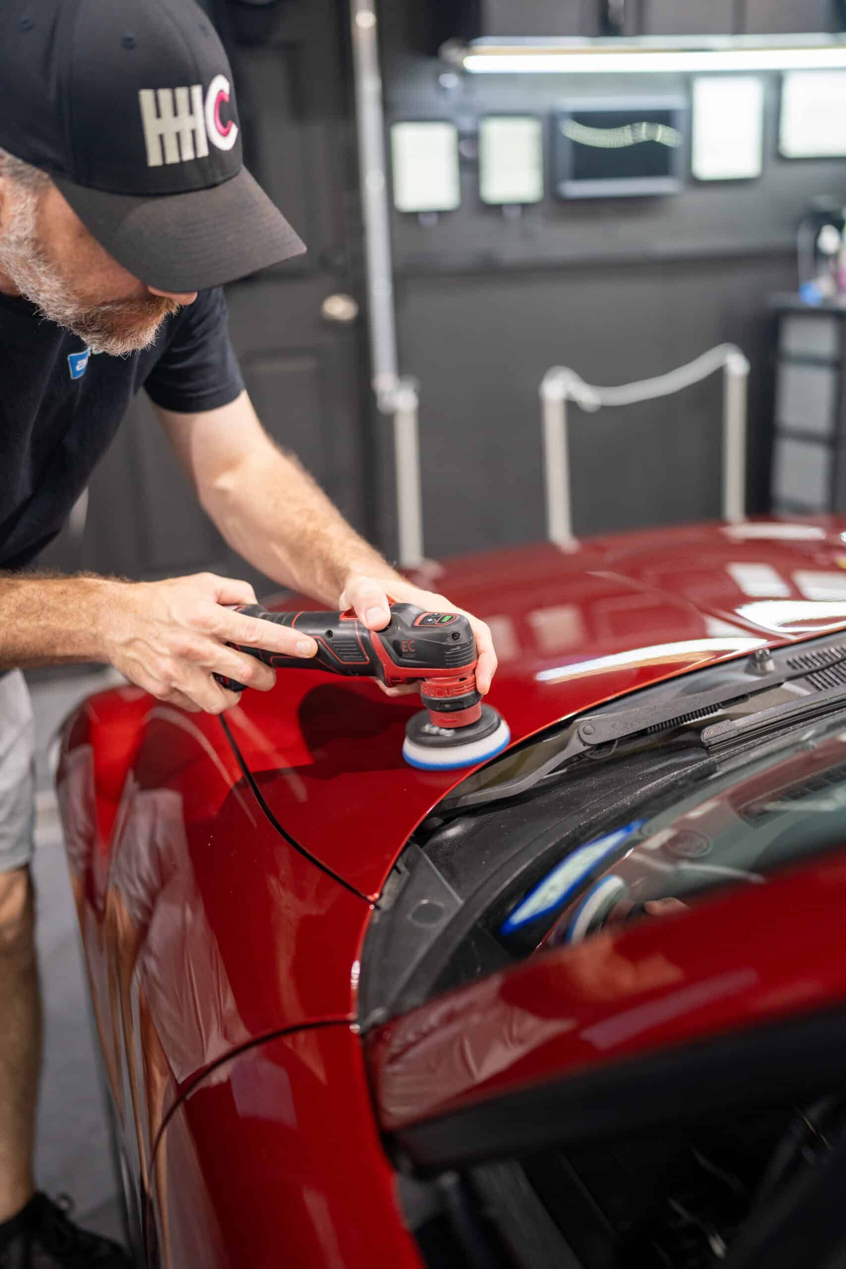 A man is polishing the hood of a red car.