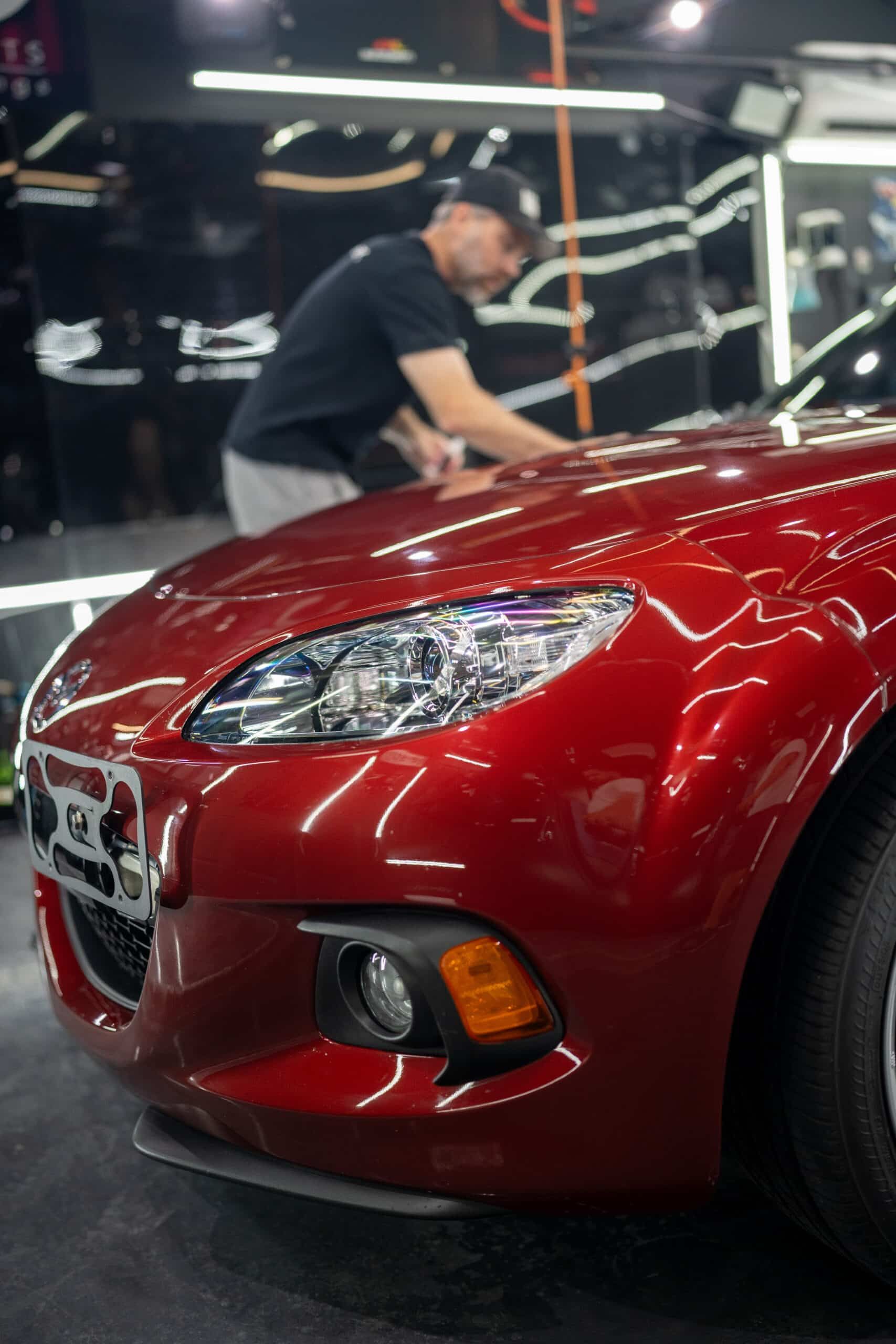 A man is working on the hood of a red car