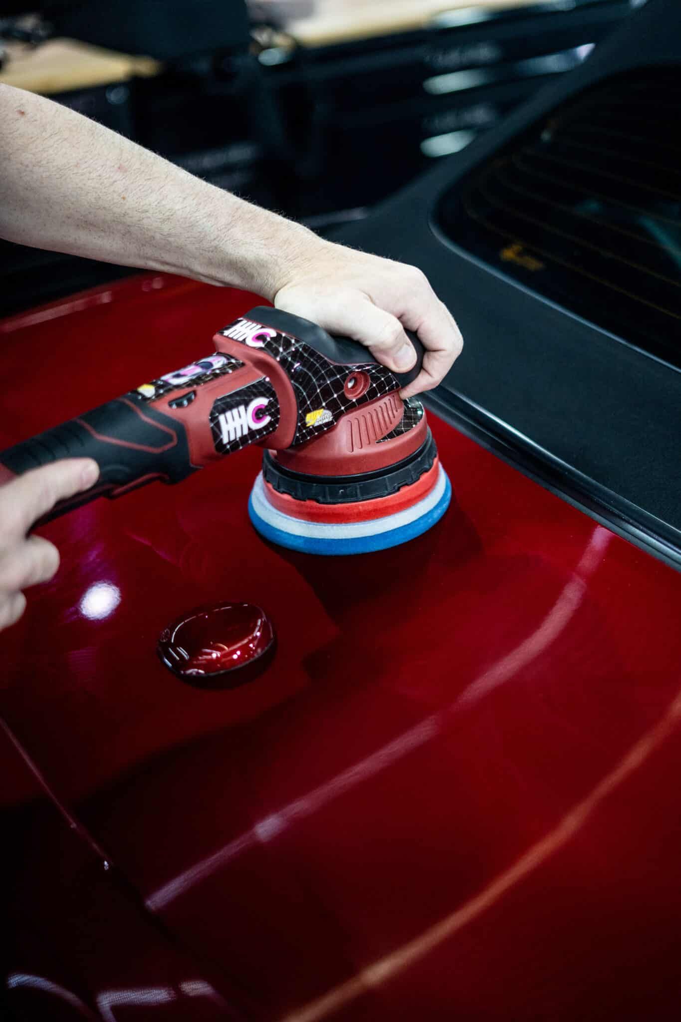 A person is polishing a red car with a machine.