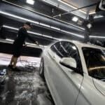 A man is washing a white car in a garage.
