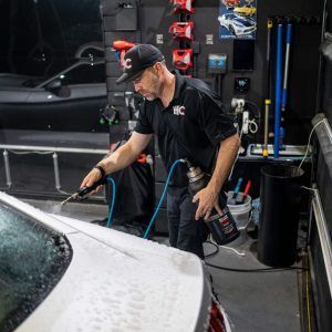 A man is washing a white car in a garage.