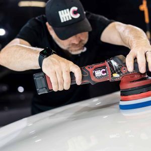 A man wearing a hat is polishing a car with a machine.