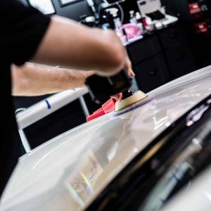 A man is polishing the hood of a white car.