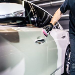 A man is cleaning the door of a car with a sponge.
