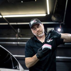 A man is cleaning a car with a sponge in a garage.
