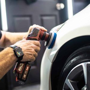 A man is polishing a white car with a polisher.