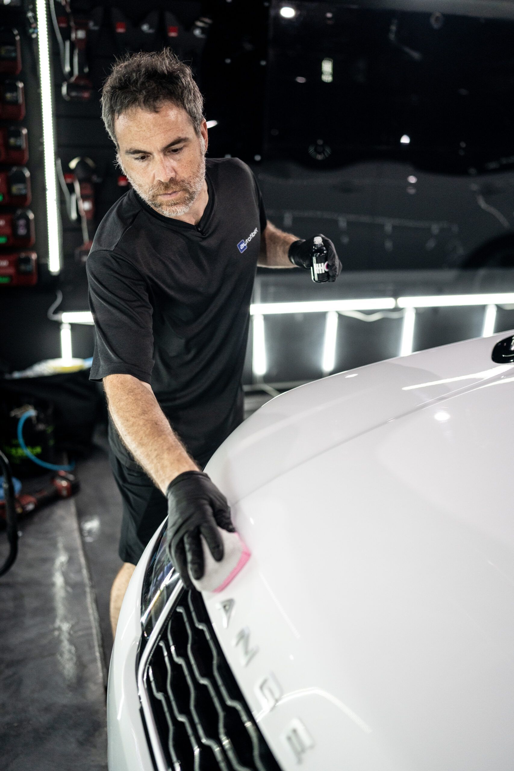 A man is polishing the hood of a white range rover in a garage.