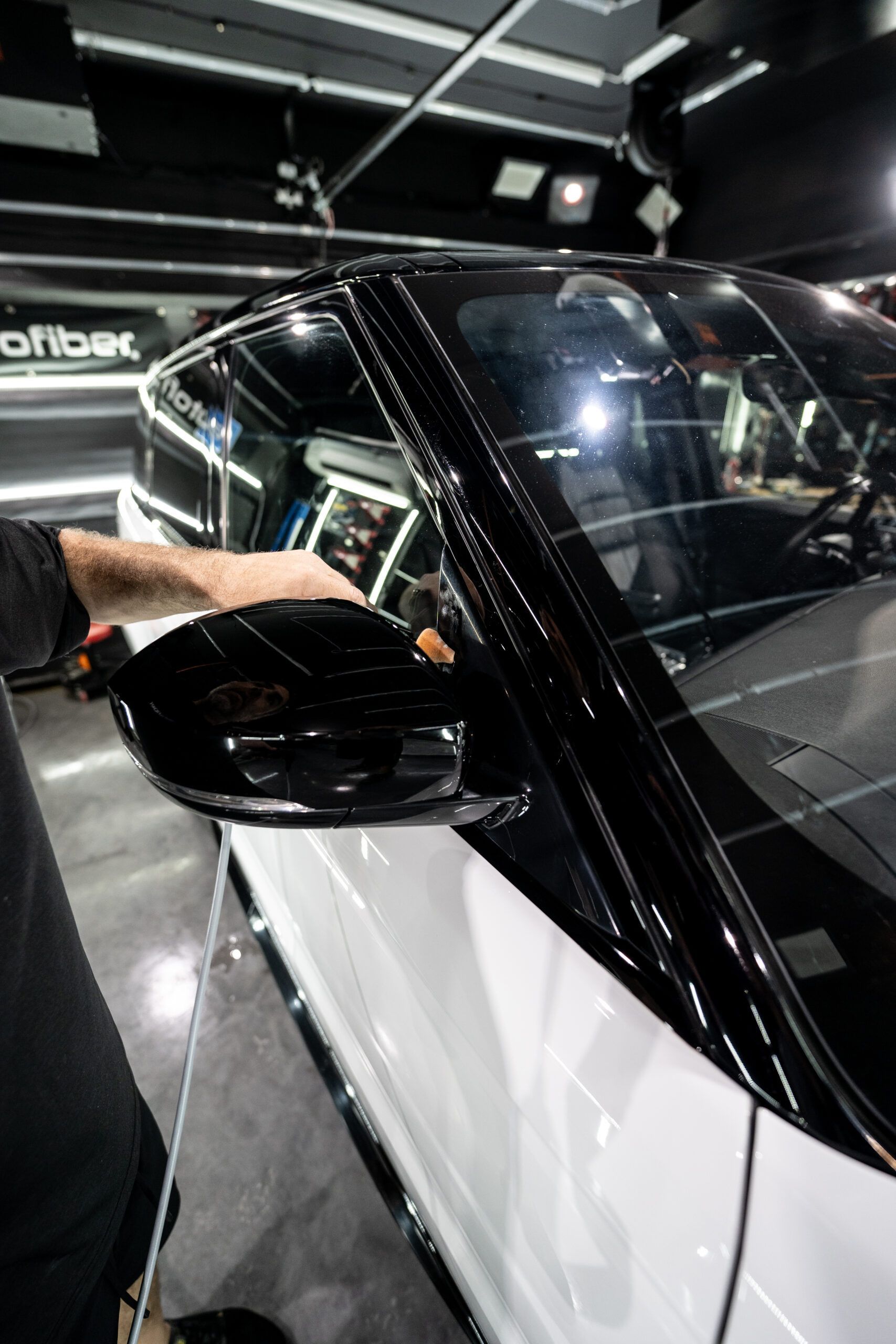 A man is cleaning the side mirrors of a white car.
