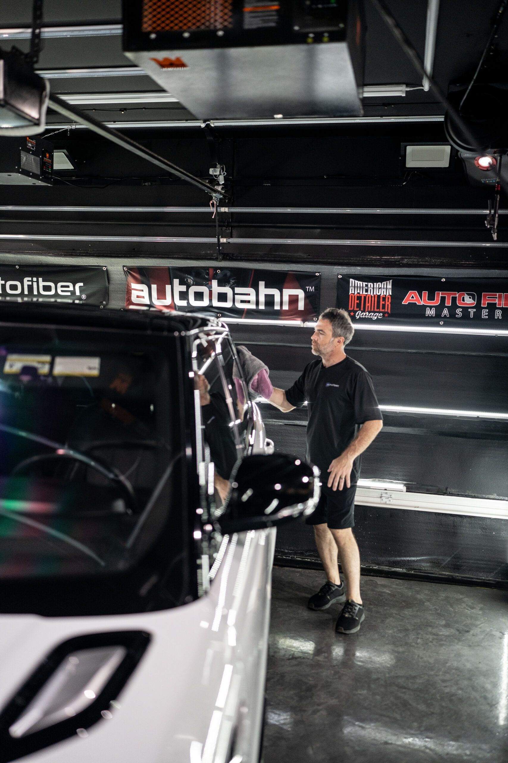 A man is standing next to a white car in a garage.