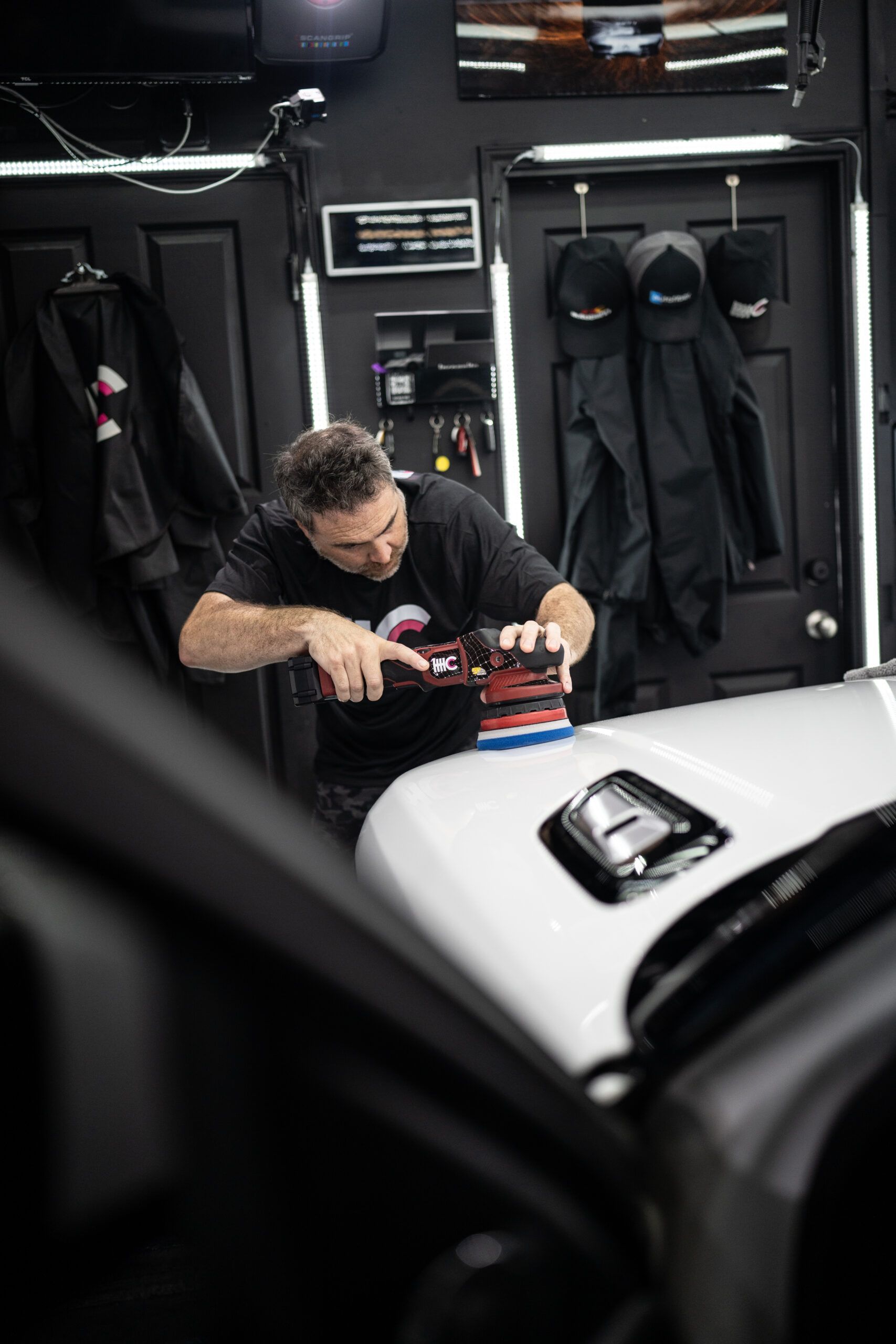 A man is polishing the hood of a car in a garage.