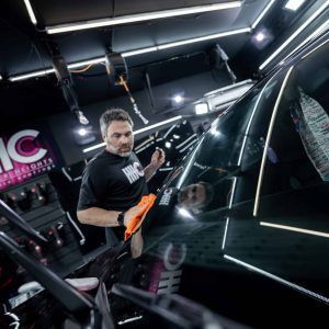 A man is cleaning the windshield of a car in a garage.