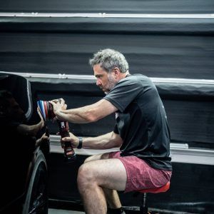 A man is sitting on a stool polishing a car.
