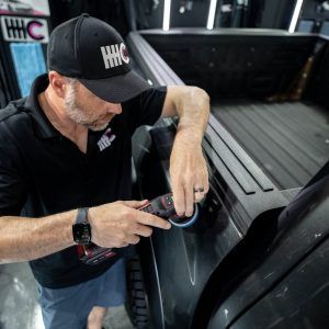 A man wearing a hhc hat is polishing the side of a truck.