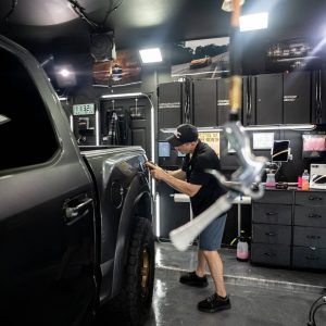 A man is polishing the fender of a truck in a garage.
