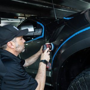 A man is polishing the side of a truck with a machine.