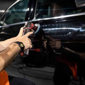 A man is polishing a black car with a machine.