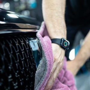 A person is cleaning the front of a car with a towel.
