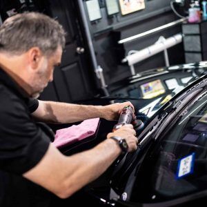 A man is polishing the windshield of a car in a garage.