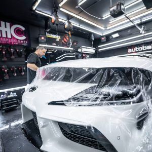 A man is covering a white car with plastic wrap in a garage.