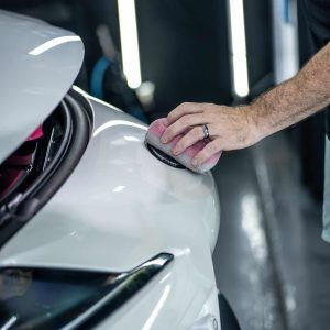 A man is polishing a white car with a sponge.