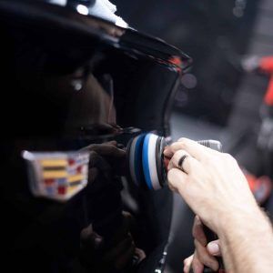 A person is polishing a black car with a polisher.