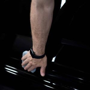 A man wearing a watch is cleaning a car door with a cloth.