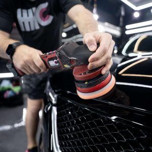 A man is polishing a black car with a machine.