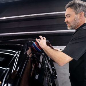 A man is polishing a black car with a polisher.