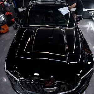 A man is cleaning the hood of a black car in a garage.