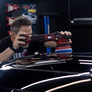 A man is polishing the roof of a car with a machine.
