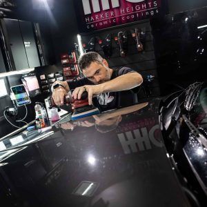 A man is polishing a black car in a garage.