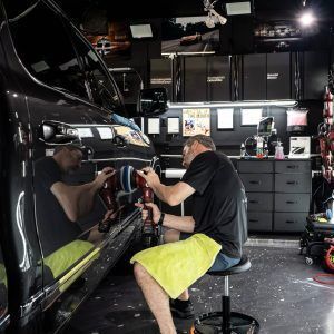 A man is polishing a black car in a garage.