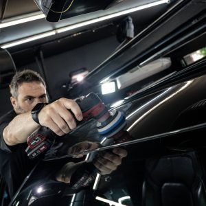 A man is polishing the roof of a car with a machine.
