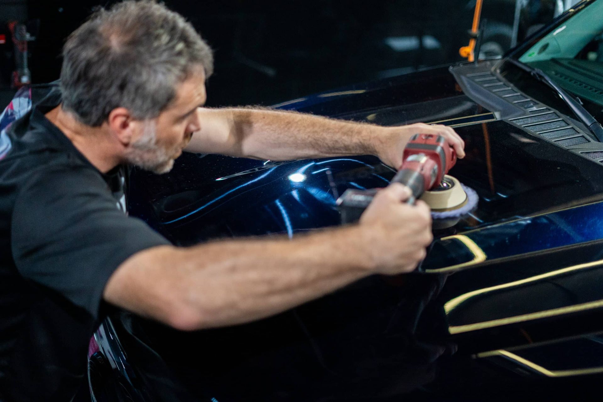 A man is polishing the hood of a car with a machine.