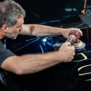 A man is polishing a black car with a machine.