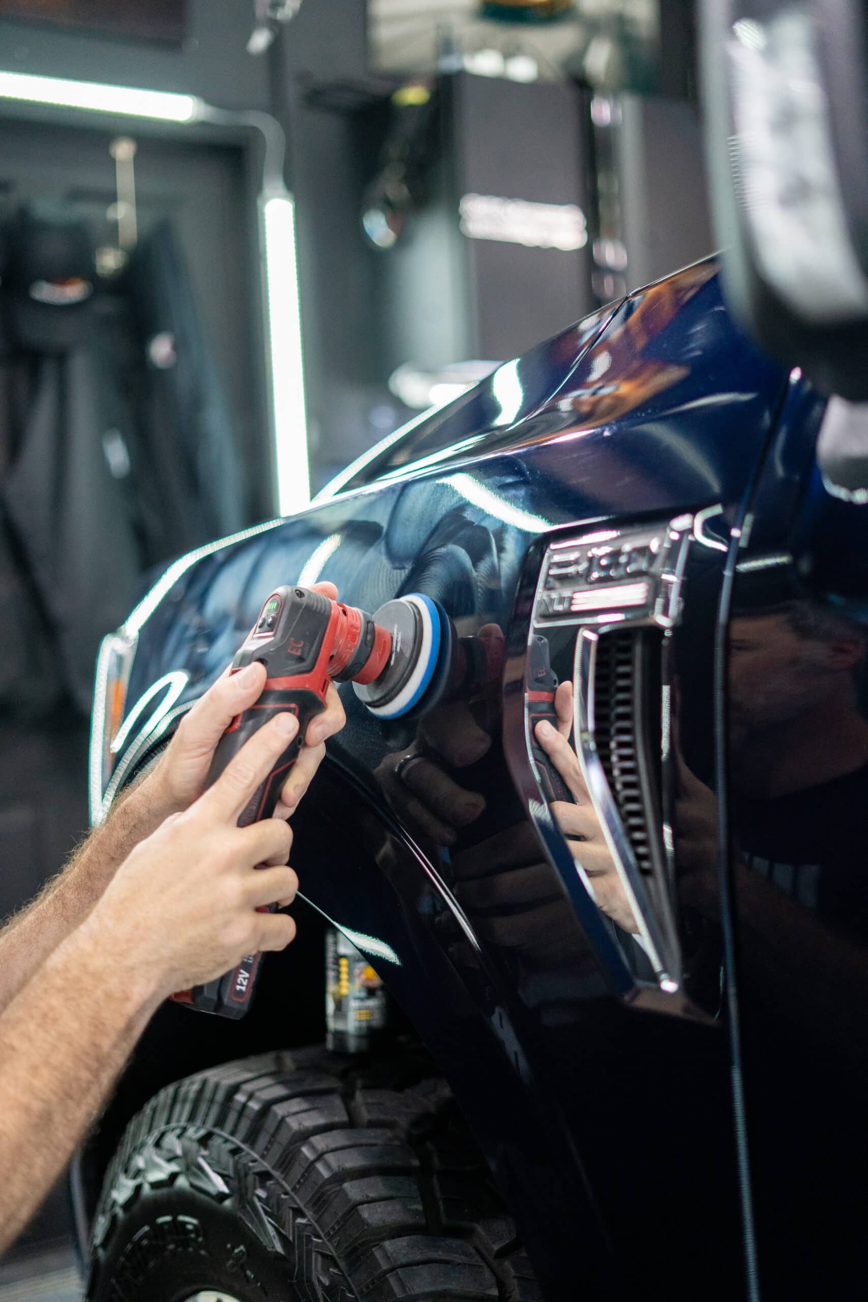 A man is polishing the fender of a truck with a machine.